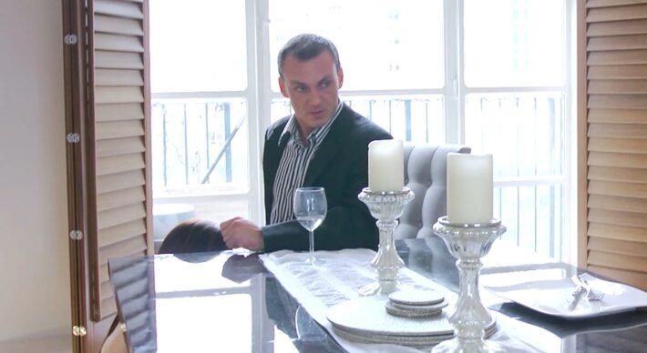 Homem tomando café sorrindo, com uma atendente ajoelhada ao lado em clima de “serviço completo”