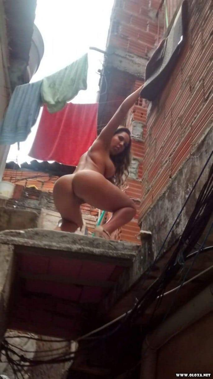 Mulher Melão nua, de salto alto na laje com vista pro morro