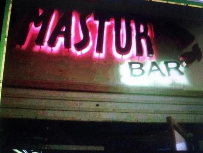 Letreiro de bar antigo com nome esquisito pintado à mão, cercado de mesas de plástico e cerveja quente