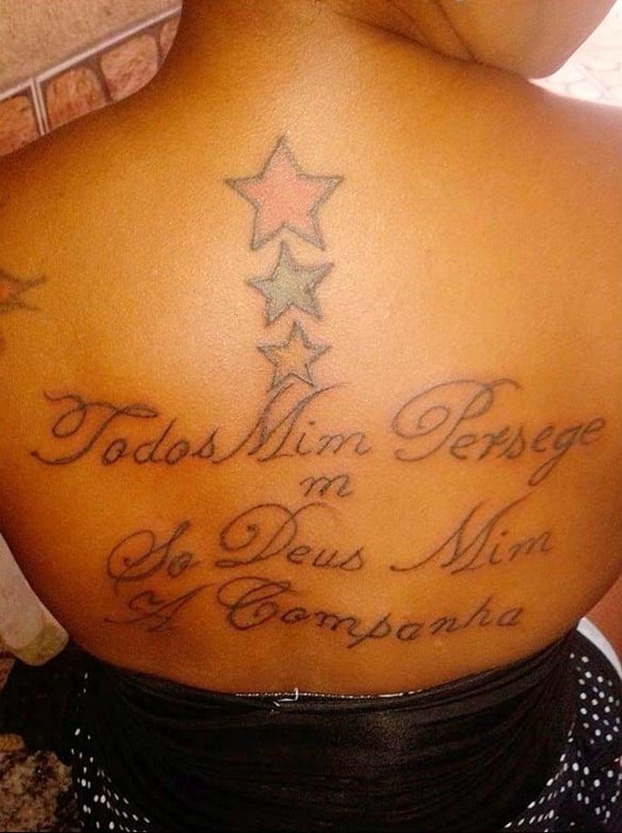 Costas de uma mulher com tatuagem mal escrita: “Todos mim persege / só Deus mim a companha”